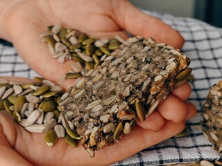 healthy bread, close-up, Lena pumpkin seeds and seeds in the palms, buckwheat bread, freshly baked, sliced, striped tablecloth, hands holding a piece of bread, heart shape