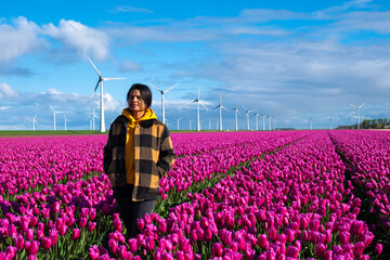A woman stands gracefully in a vast field of purple tulips, surrounded by the beauty of spring in...