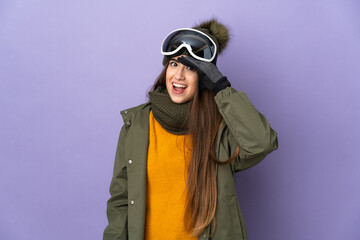 Skier caucasian girl with snowboarding glasses isolated on purple background doing surprise gesture while looking to the side