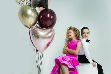 curly-haired girl and a boy engaged in ballroom dancing pose with balloons in a photo studio