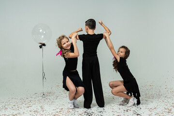 two curly-haired girls are hanging on the boy's arms showing his strength