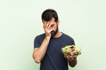 Young handsome man with salad over isolated green wall with tired and sick expression