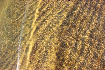 Close-up of a river bed with yellow sand, stones curling from the wave, in bright sunlight with beautiful highlights on the water. Texture of river sand. Texture with seashells and pebbles on the wet 