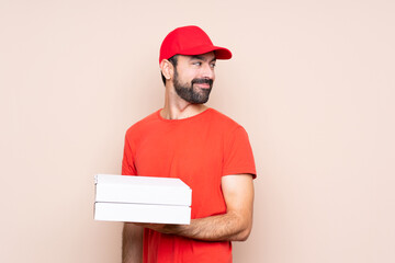 Young man holding a pizza over isolated background with arms crossed and happy