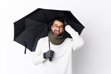 Caucasian handsome man with beard holding an umbrella over isolated white wall with an expression of frustration and not understanding