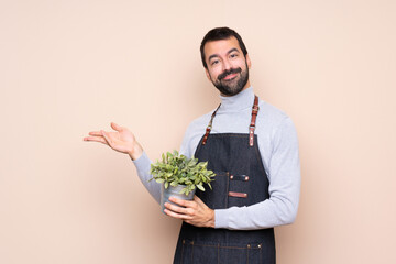 Man holding a plant over isolated background extending hands to the side for inviting to come