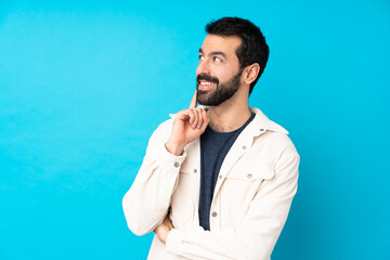 Young handsome man with white corduroy jacket over isolated blue background thinking an idea while...