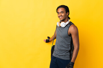 Young sport African American man with braids with bag isolated on yellow background extending hands...