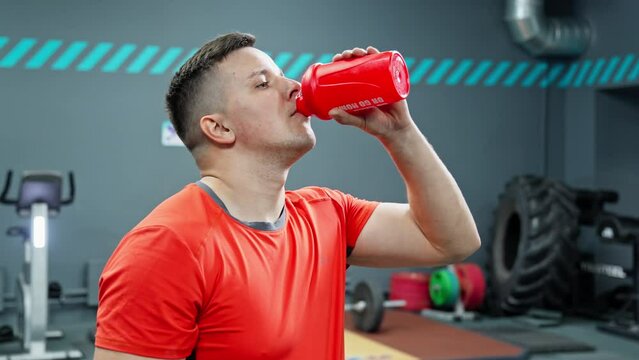 Sportsman drinking protein shake in gym. Athlete drinking water during break. Workout and healthy lifestyle concept. Man taking a break during training. 4K, UHD