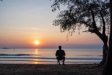 Man sit on a chair on the beach with beautiful sea and sunrise sky, .Outdoor lifestyle concept.