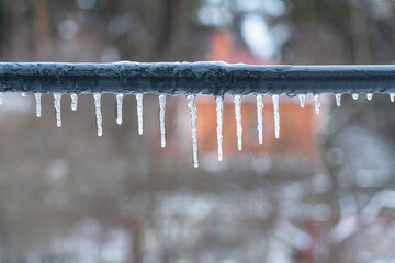 Several icicles of different lengths hang from the gray pipe of the crossbar. A blurry rural...