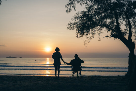 Tourist couple on the beach under the tree and watch the sunrise,  colorful golden morning light, Outdoor lifestyle concept.