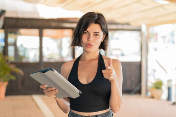 Young pretty Bulgarian woman holding a tablet at outdoors surprised and pointing front
