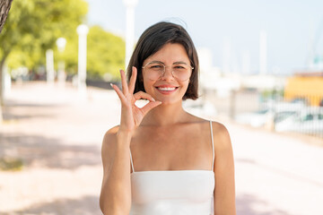 Young pretty Bulgarian woman with glasses at outdoors showing ok sign with fingers