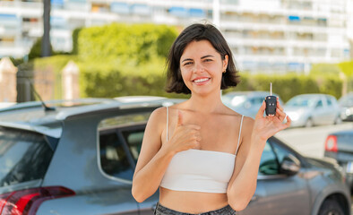 Young pretty Bulgarian woman holding car keys at outdoors with thumbs up because something good has happened