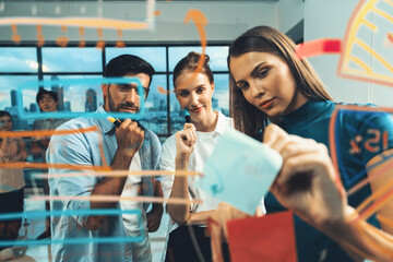 Skilled project manager pointing at glass wall while coworker thinking about plan. Diverse business team working together, brainstorming marketing idea or business plan. Creative start up. Tracery.