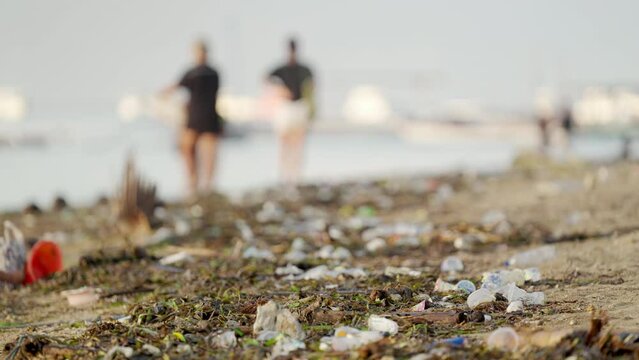 Environmental issue, plastic pollution on bali beach with blurred tourists in background