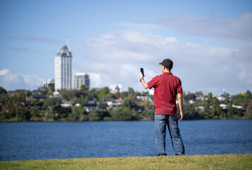 Man taking photos of lake Pupuke and Takapuna skyline. Takapuna, Auckland.