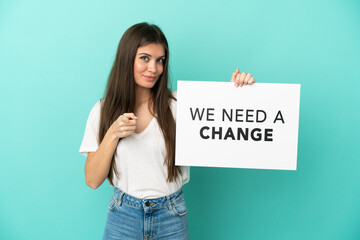 Young caucasian woman isolated on blue background holding a placard with text We Need a Change and pointing to the front - 790669143