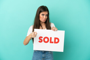 Young caucasian woman isolated on blue background holding a placard with text SOLD and pointing to the front - 790669158
