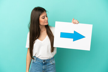 Young caucasian woman isolated on blue background holding a placard with arrow symbol - 790669160