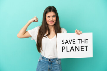 Young caucasian woman isolated on blue background holding a placard with text Save the Planet and doing strong gesture - 790669161