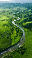 A mountain river meanders through vibrant green fields, creating a picturesque scene of natural beauty. The lush greenery contrasts against the clear blue waters, a stunning view from a helicopter