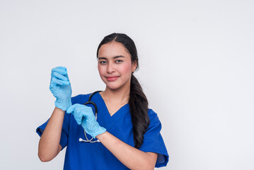 Asian female caregiver in blue scrubs putting on medical gloves, isolated on white