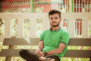 Young handsome Indian man sitting on bench in the park.