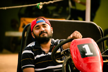 Young Indian guy sitting on go-karting vehicle, ready to race. - obrazy, fototapety, plakaty