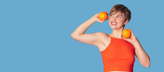 Smiling slender Caucasian girl with citrus oranges in her hands. Panoramic banner, free space....