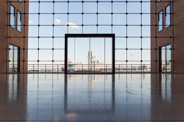 Looking through a vast, contemporary glass window, a prominent glass door sits centrally, flanked...
