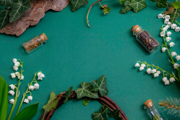 Kompozycja na stole na zielonym tle w otoczeniu roślinności: bluszcz, konwalie. 