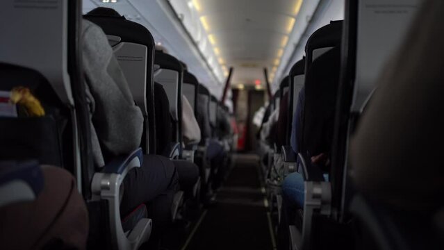 View of aisle pathway on airplane with passengers on seats. Unrecognisable passengers sitting in chairs on the plane. Video can be used for your video.