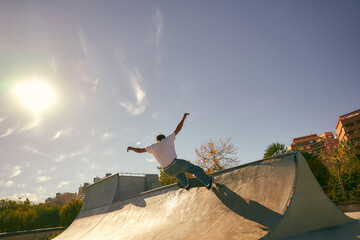 Back view of young skateboarder flies with his board on the ramp of a skate park