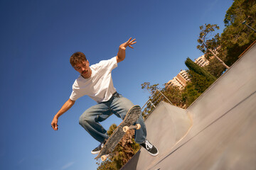 Excited young man riding skateboard in skate park on sunny day. Extreme sport concept