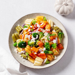 Autumn pasta salad with roasted pumpkin, broccoli, feta cheese on bright light background, fall season salad