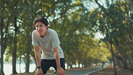 Tired runner asian man breathing after run marathon in public park. Young male athlete have break after running exercise in summer park. Sport man resting after workout outdoor.