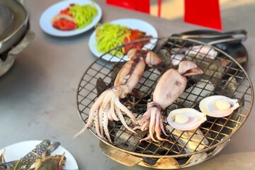 Freshly grilled squid and scallops on mesh grill, with glimpse of street vendor's bustling seaside...