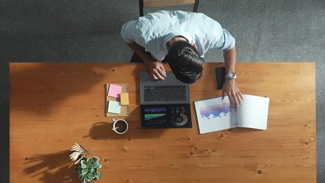 Top aerial view of manager working on laptop while looking at data analysis. Leader compare financial statistic graph while making decision at meeting table with document scatter around. Convocation.