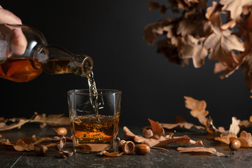 Whiskey on a black table with dried-up oak leaves.