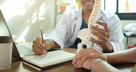 close up physical therapist hand pointing on human skeleton at low back to advise and consult to patient to treatment at office for healthcare concept