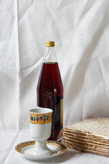 Vertical photo of stack of matzah, a Kiddush cup, and a bottle of grape juice against a backdrop of white lace curtains, is typically consumed during the celebration of Passover. Jewish Passover meal