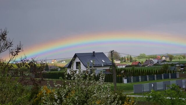 A vivid rainbow prominent on the sky over small village houses