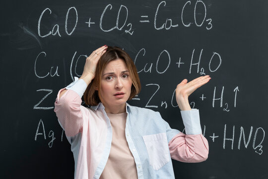 Confused female student writing the formula of a chemical reaction on the blackboard