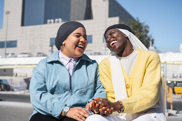 Two happy muslim women friends holding hands having fun laughing in the city