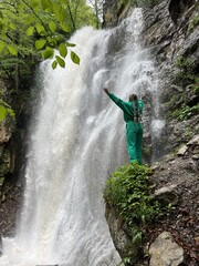 A woman on the background of the Lyazhginsky waterfall in the spring forest. A cascading waterfall surrounded by greenery. Splashes of water. The water flows along the Lyazhgi River. Ingushetia