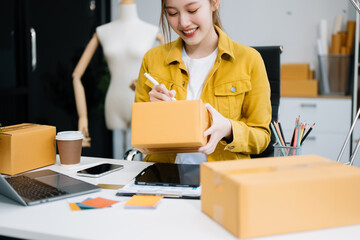 Young business owner woman prepare parcel box and standing check online orders for deliver to...