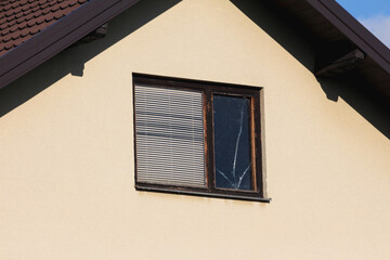 Attic window with dilapidated cracked wooden frame and closed window blinds on left and broken...