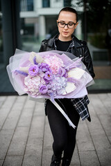 Cute young woman in glasses looks at a large bouquet of purple flowers in her hands